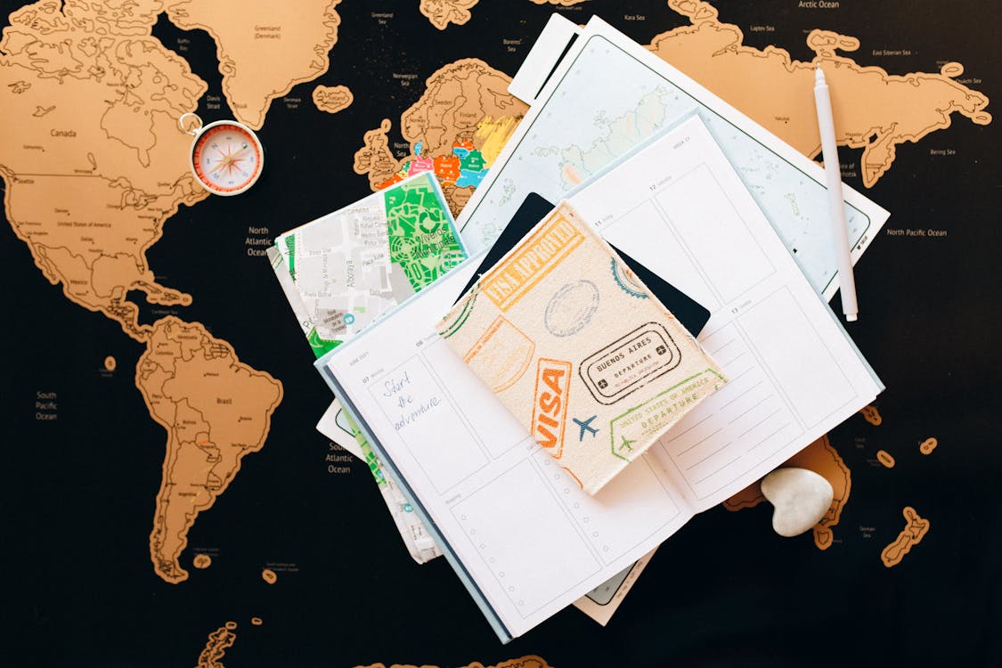 Passport with visa stamps on a world map with travel planner and compass - sabbatical health insurance planning